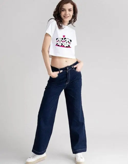 Person wearing a white crop top with a graphic design and dark blue jeans on a plain background

