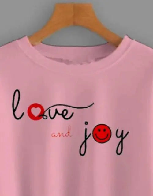 Pink sweatshirt with 'love and joy' text and smiley face on a hanger against a gray background

