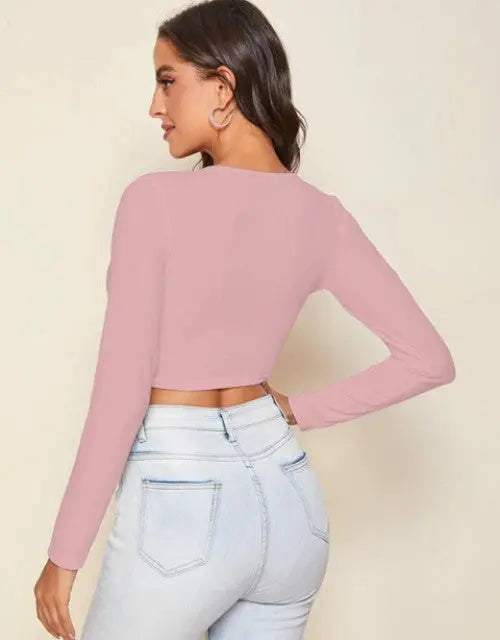 Woman wearing a pink long-sleeve crop top and light blue jeans on a beige background

