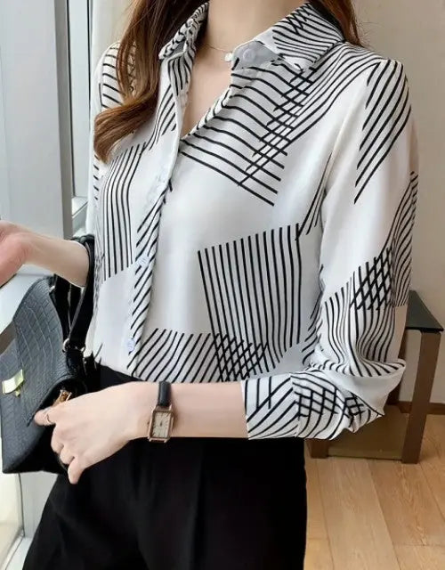 Person wearing a black and white patterned blouse holding a black handbag indoors.