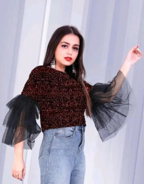Woman wearing a black and red top with sheer sleeves against a white curtain background