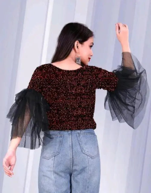 Woman wearing a red sequin top with black tulle sleeves against a white curtain background