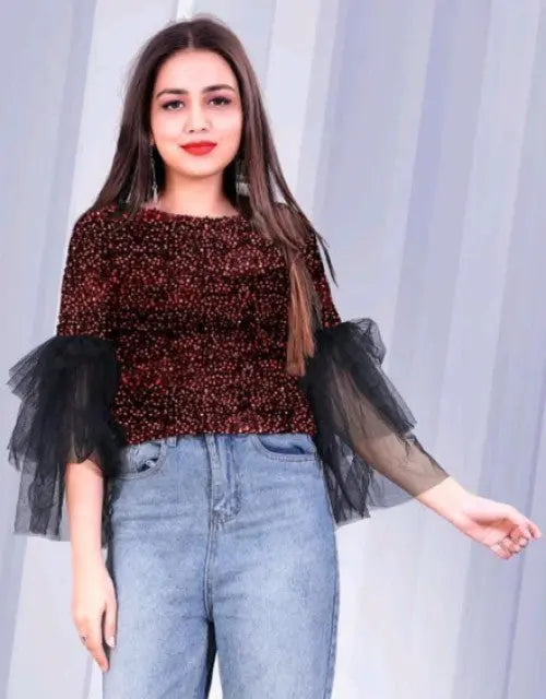 Woman wearing a brown top with sheer black sleeves against a light curtain background