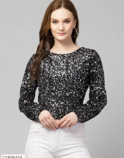 Woman wearing a black sequin top and white pants on a gray background