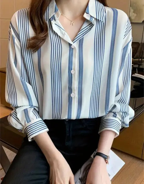 Person wearing a white shirt with blue vertical stripes sitting indoors.