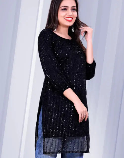 Woman wearing a black sequined top against a light curtain background