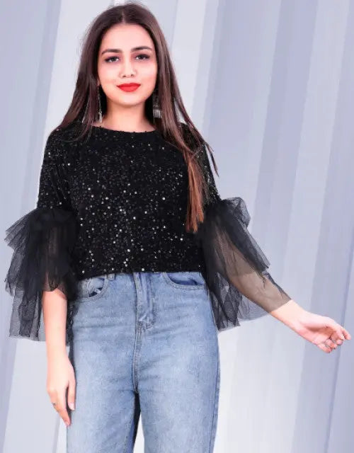 Woman wearing a black sequin top with sheer sleeves against a light gray background
