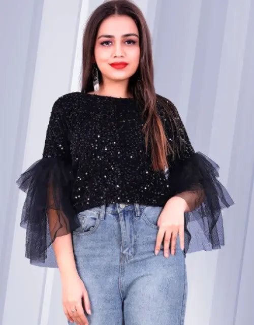 Woman wearing a black sequin top with sheer sleeves against a light gray curtain background