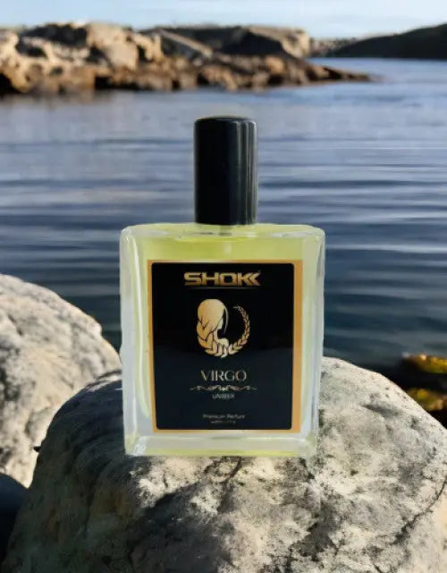 Perfume bottle labeled 'SHOK' with 'Virgo' on a rock by a body of water

