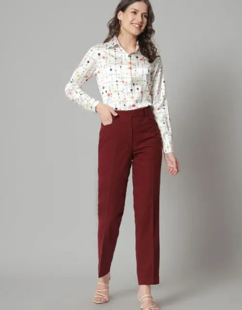Woman wearing a patterned blouse and maroon pants on a gray background